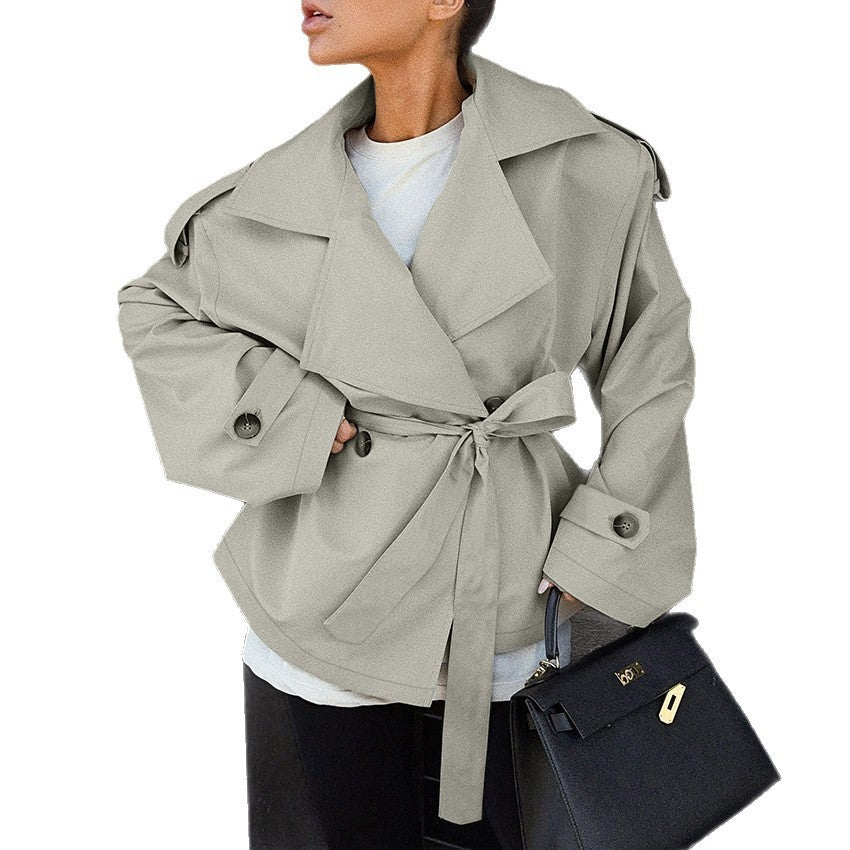Person wearing a light gray trench coat with a black handbag on a white background