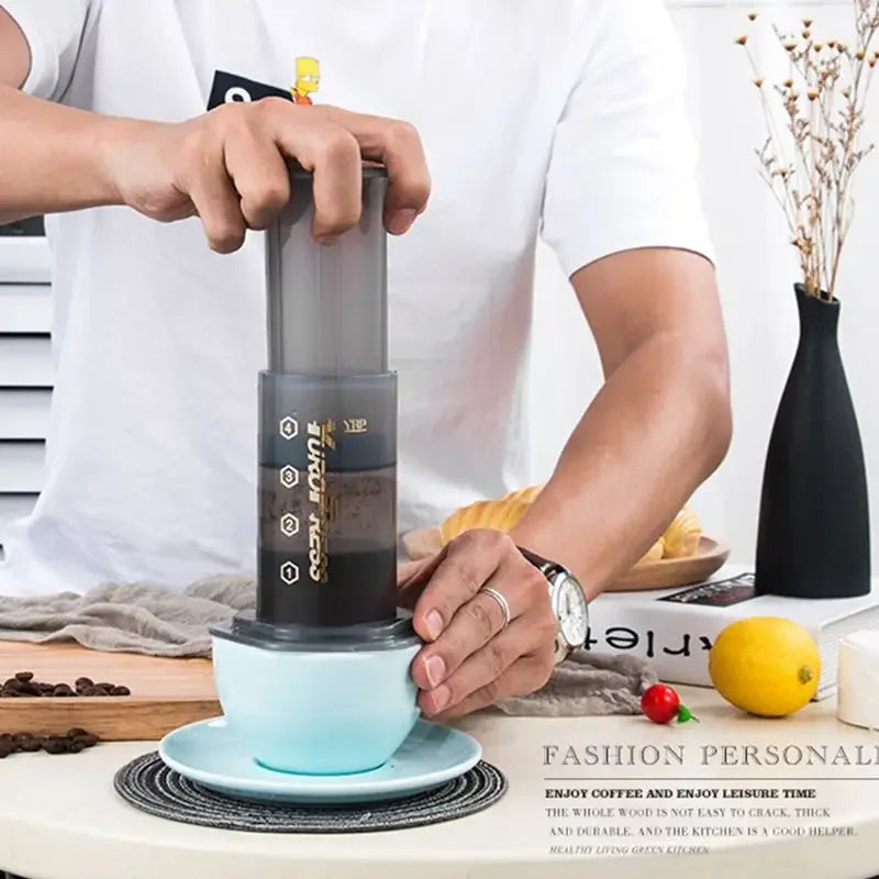 Person using a portable coffee maker with a cup on a table.
