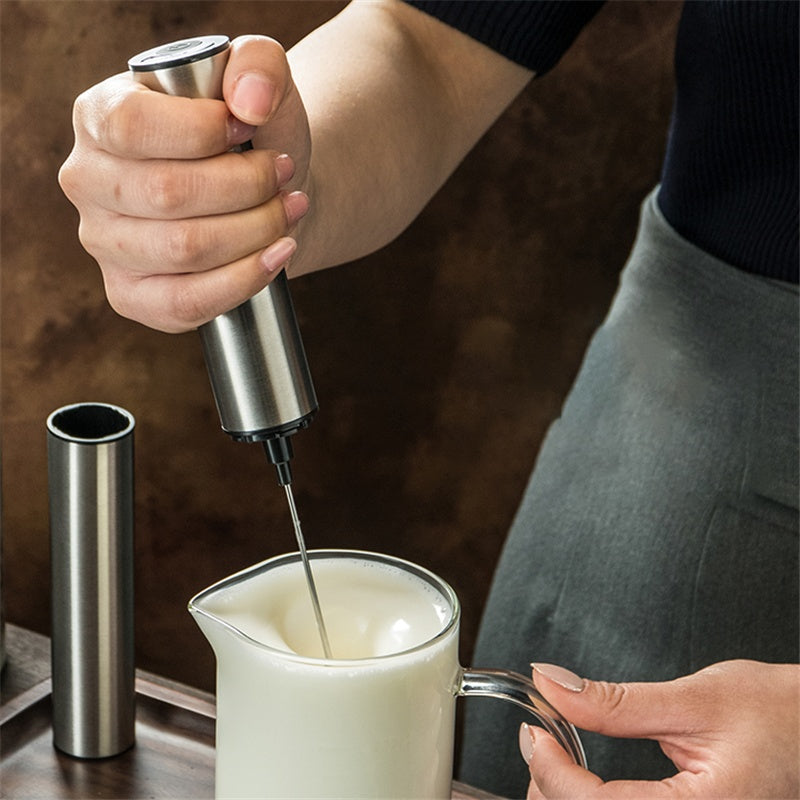 Person using a milk frother to froth milk in a small pitcher.