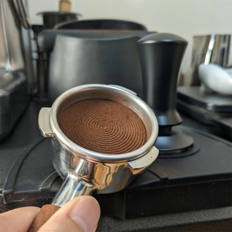 Coffee grounds in a silver tamper held over a coffee filter on a coffee machine.