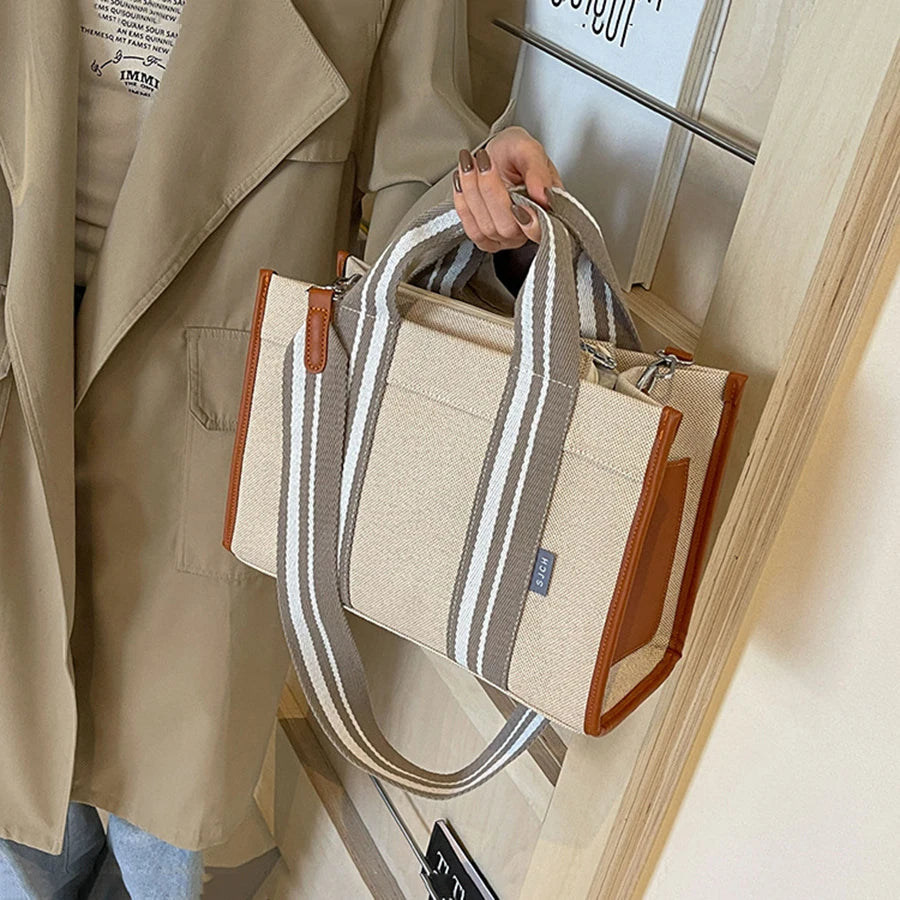 Person holding a beige tote bag with brown accents and striped handles.