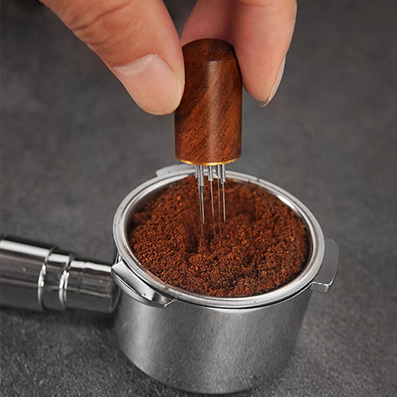 Hand using a wooden tool to compress coffee grounds in a metal grinder.