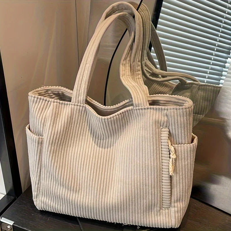 Beige corduroy tote bag with multiple pockets on a reflective surface.