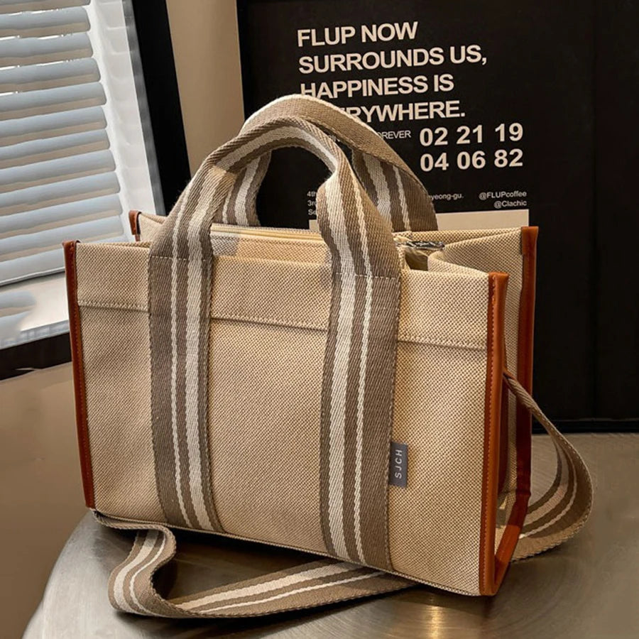 Beige handbag with striped handles on a reflective surface, with a blurred background.