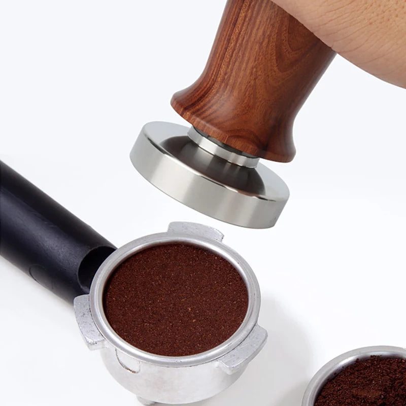 Coffee tamper pressing coffee grounds into a portafilter on a white background