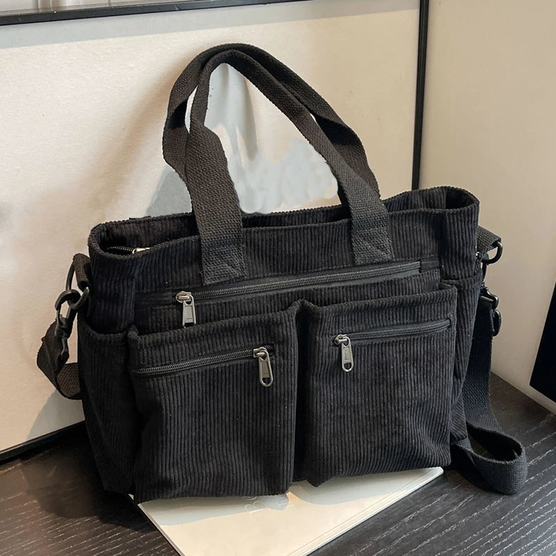 Black corduroy handbag with multiple pockets on a wooden surface.