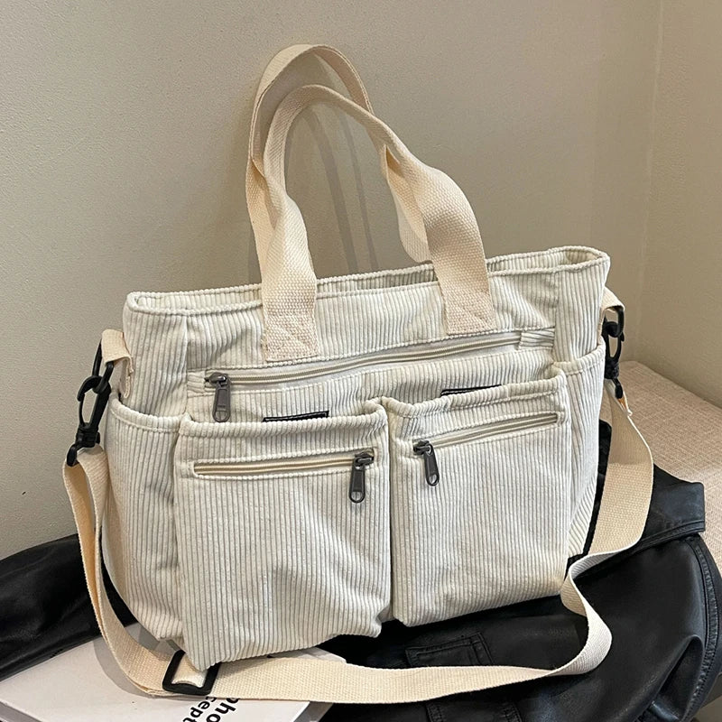 Light gray tote bag with multiple pockets and straps on a neutral background