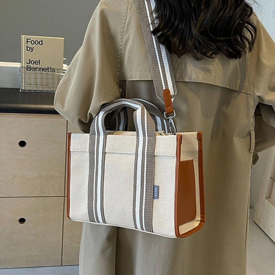 Person holding a striped handbag with brown accents in an indoor setting