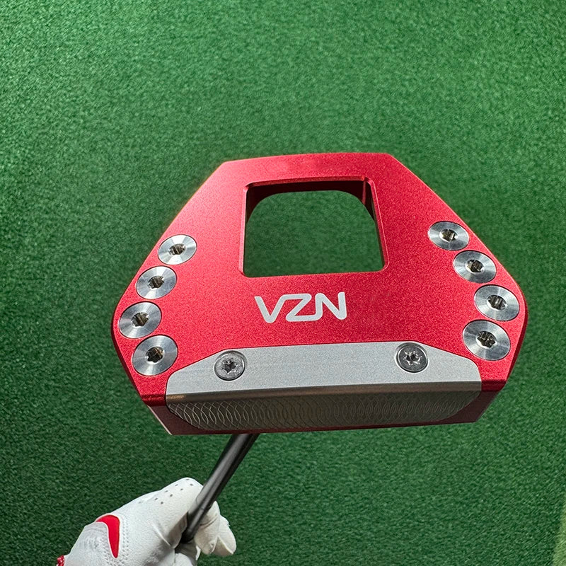 beginner golf putter UK - A red VZN golf putter head with silver screws and a silver face plate, held by a gloved hand against a green turf background.