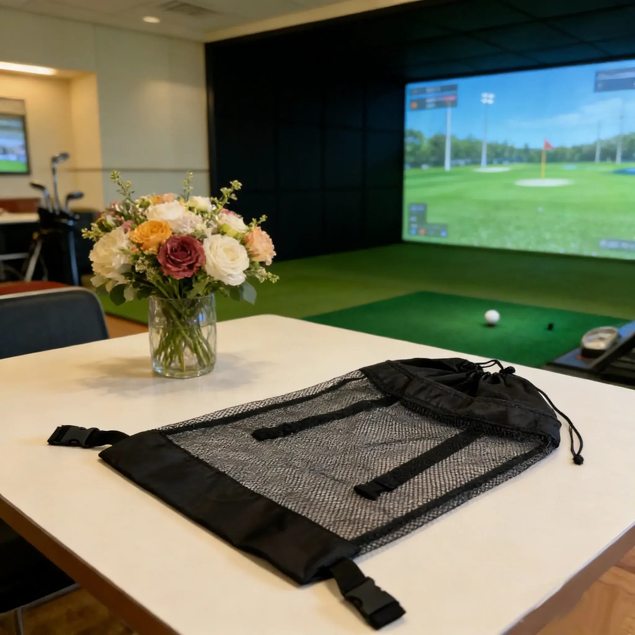 Black mesh bag on a table with a bouquet of flowers in the background, featuring a golf simulator.