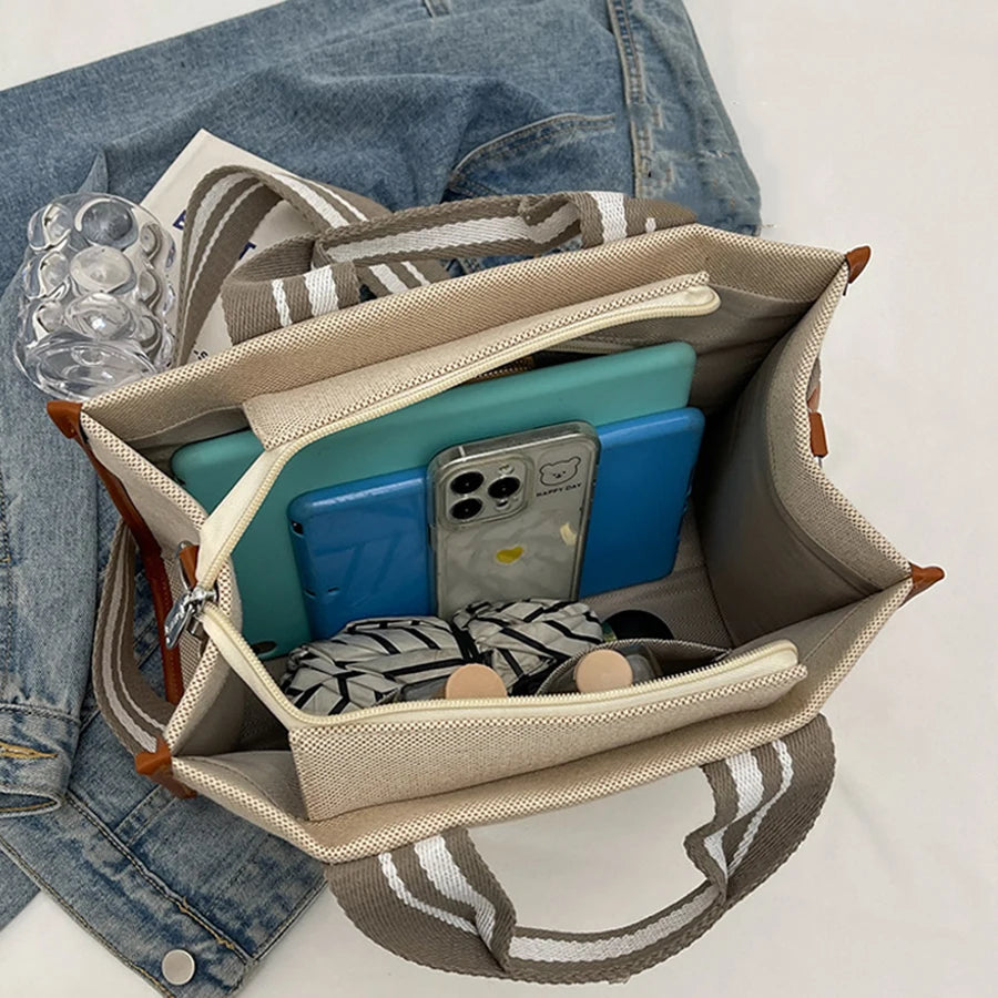 Open beige bag with electronic devices and clothing on a white background