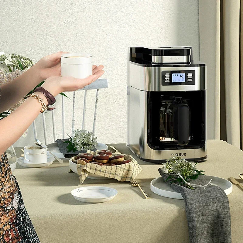 Person holding a coffee cup near a coffee machine on a table with a light-colored background