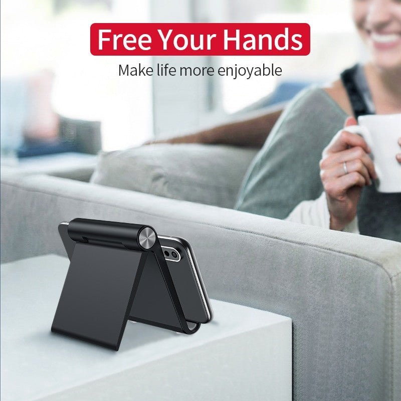 Black Olaf foldable desktop mobile phone holder stand on a table, supporting an iPhone, with a relaxing home background and text "Free Your Hands – Make life more enjoyable."