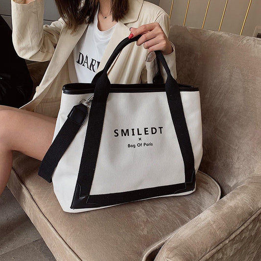 A model sitting on a sofa holding new Fashion Canvas Women Handbags - Stylish crossbody bag and tote messenger bags.